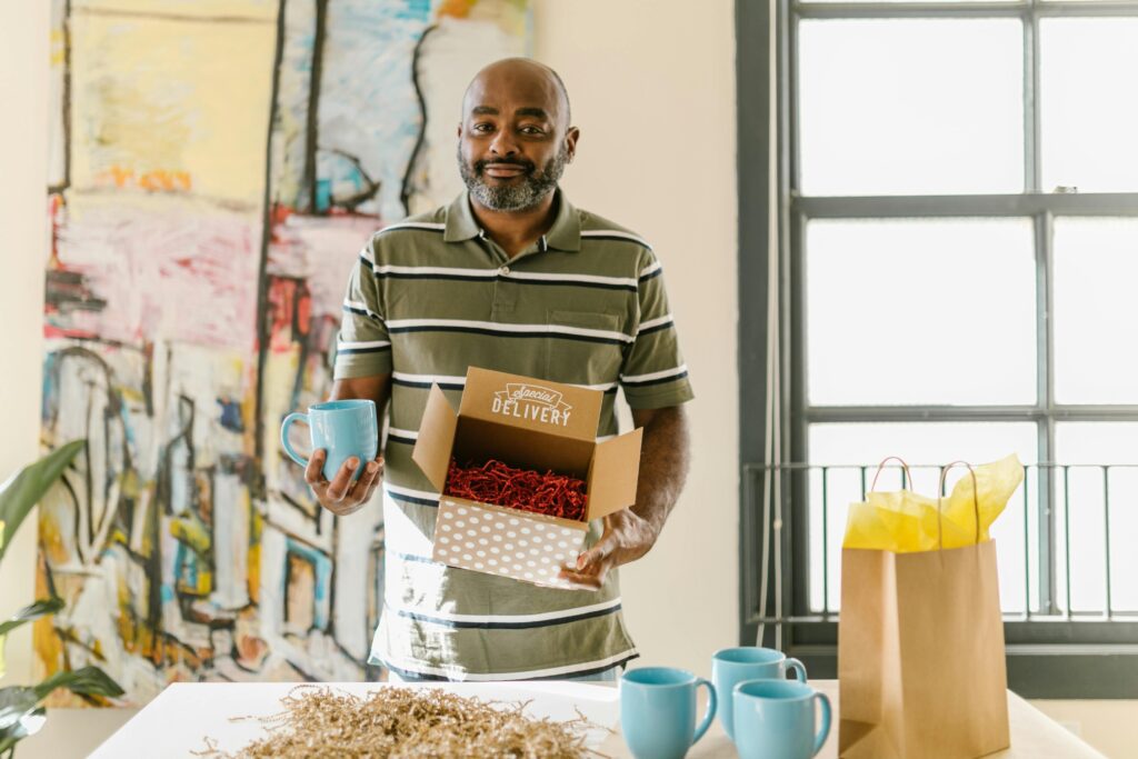 pexels-photo-7310197-7310197 Man packing blue coffee mugs for delivery in a bright, artistic workspace.